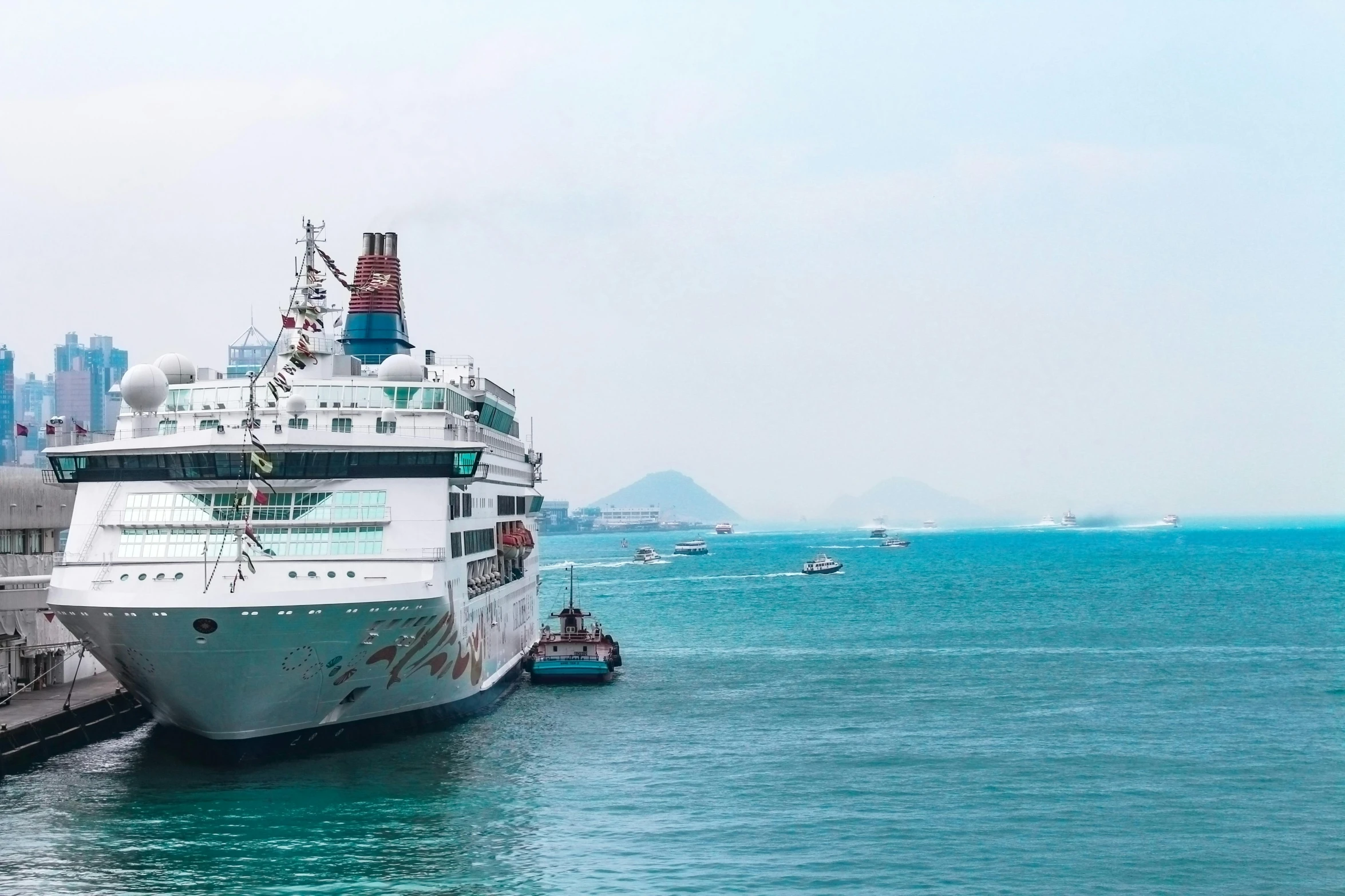 a cruise ship docked at a dock with a city in the background, pexels contest winner, a still of kowloon, a ship on a deserted island, boats, splash of color