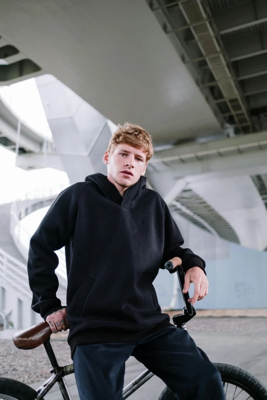 a young man sitting on top of a bike, a portrait, inspired by Cam Sykes, unsplash, black hoodie, soccer players timo werner, thumbnail, confident looking