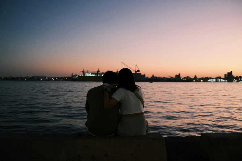 a couple sitting next to each other in front of a body of water, pexels contest winner, romanticism, harbour, early evening, embracing, in the distance