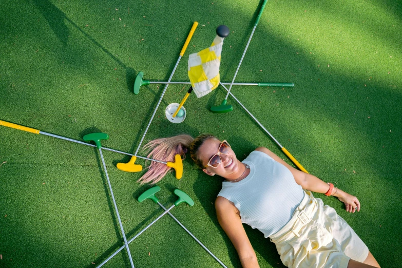 a woman laying on top of a green golf course, inspired by Shirley Teed, scattered props, yellow carpeted, avatar image