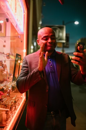a man standing in front of a store holding a cell phone, pexels contest winner, happening, jordan peele's face, wilson fisk, vibrant lights, in love selfie