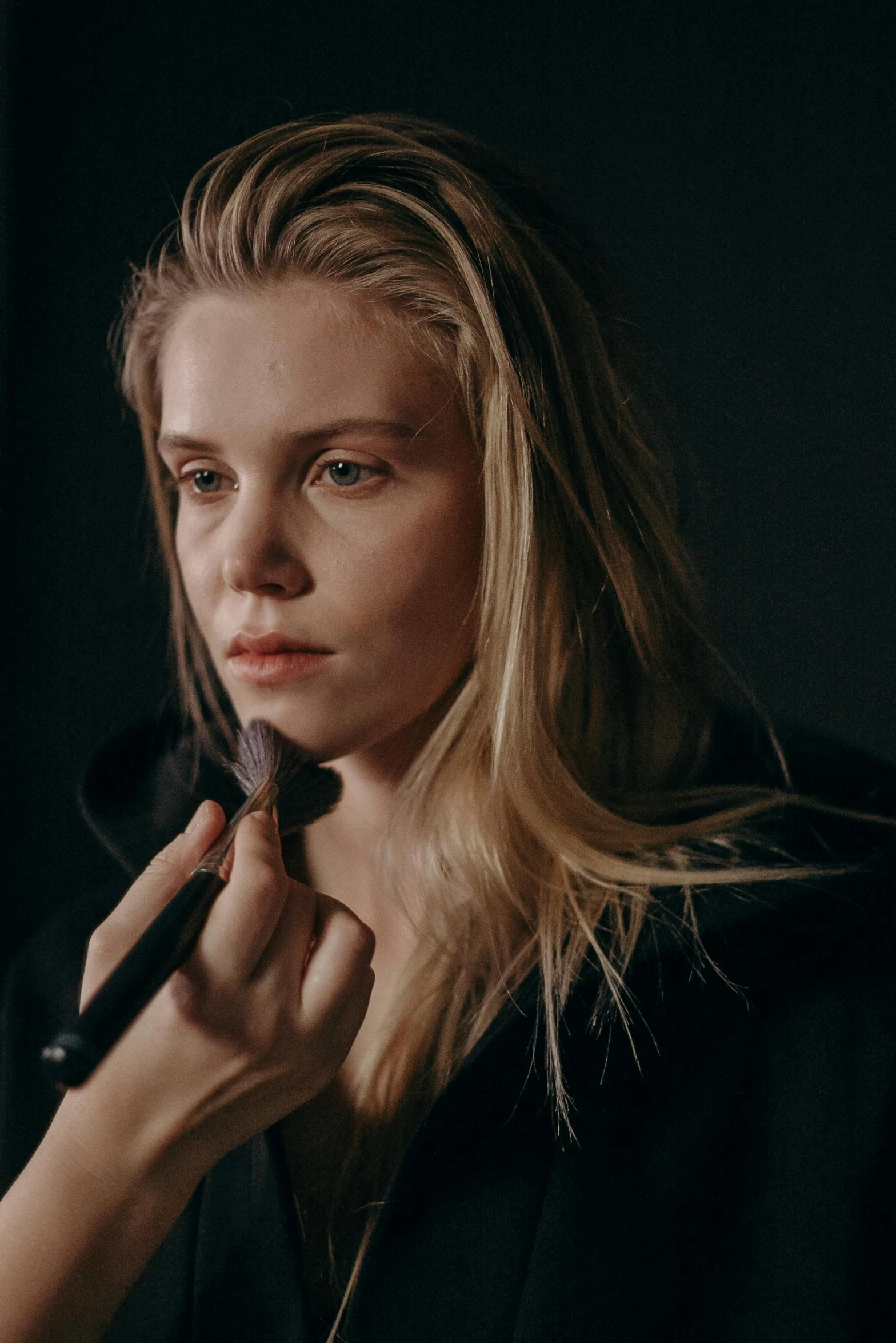 a woman brushes her hair in front of a mirror, a character portrait, inspired by Louisa Matthíasdóttir, reddit, anya taylor - joy vampire queen, in a dark studio room, in professional makeup, a blond