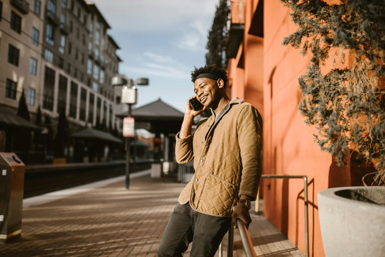 a man standing on a sidewalk talking on a cell phone, by Carey Morris, pexels contest winner, brown skin man with a giant grin, warm coloured, phone wallpaper, standing on a rooftop