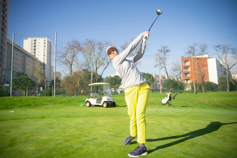 a woman swinging a golf club at a golf course, inspired by Luis Molinari, pexels contest winner, happening, yellow overall, in spain, avatar image, teenager