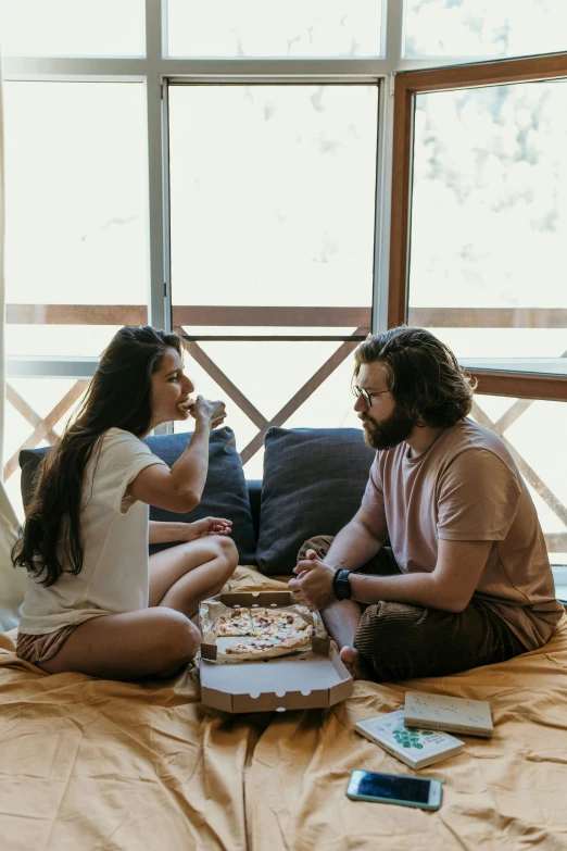 two people sitting on a bed eating pizza, with backdrop of natural light, flirting, eating cakes, cottagecore hippie