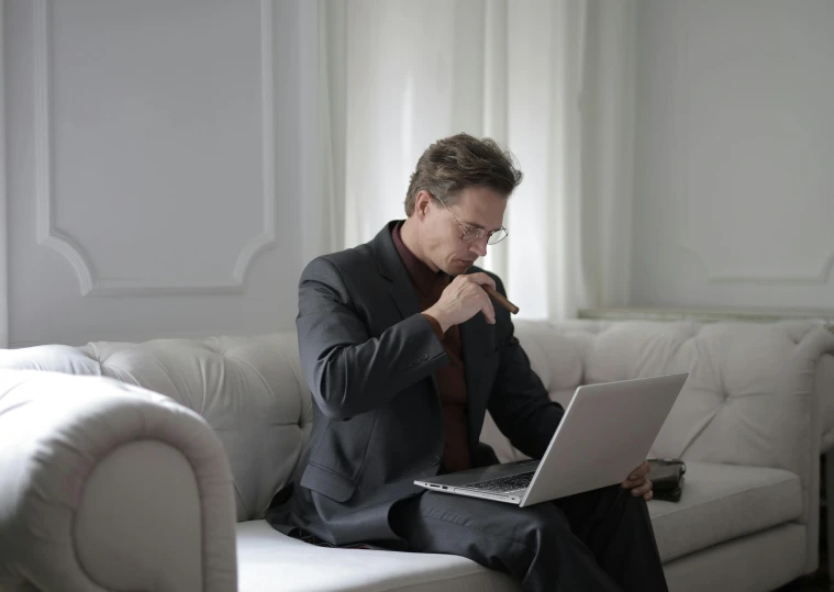 a man sitting on a couch using a laptop computer, pexels, formal attire, smoking a pipe, paul barson, eating