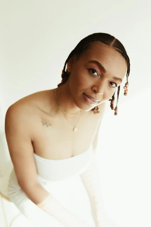 a woman in a white dress sitting on a bed, an album cover, inspired by Sophia Beale, trending on pexels, antipodeans, cornrows, headshot portrait, white backdrop, looking happy