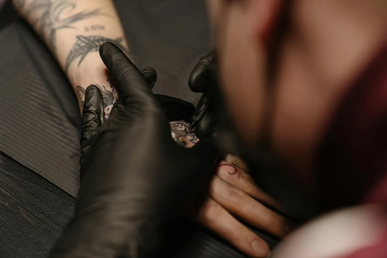 a man getting a tattoo on his arm, a tattoo, by Adam Marczyński, trending on pexels, hyperrealism, hand on his cheek, filling the frame, gloves and jewelry. motion, low quality photo