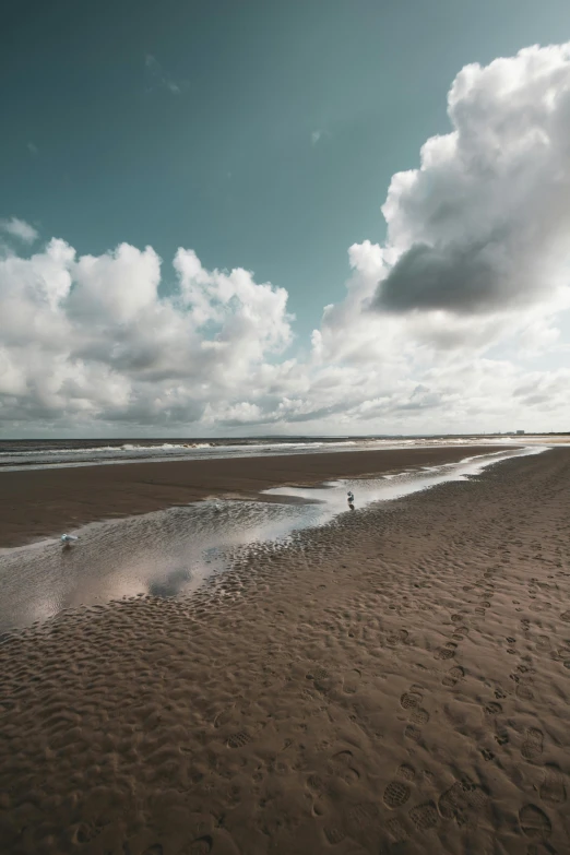 a man riding a surfboard on top of a sandy beach, helmond, scattered clouds, unsplash 4k, large scale photo