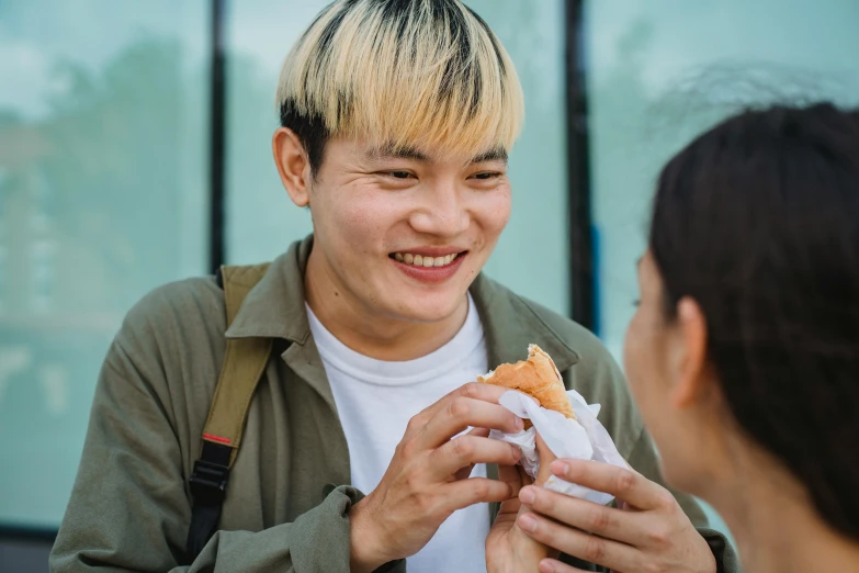 a man eating a sandwich next to a woman, pexels contest winner, bao phan, smiling male, non-binary, bun )