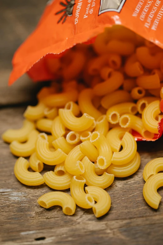 a bag of pasta sitting on top of a wooden table, unsplash, photorealism, yellow-orange, licking out, cheerios, close up