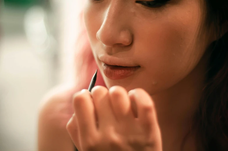 a close up of a woman putting on lipstick, trending on pexels, hyperrealism, holding pencil, dewy skin, thoughtful, asian women