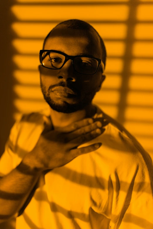 a man with glasses standing in front of a window, an album cover, inspired by Theo Constanté, warm yellow lighting, ((portrait)), teddy fresh, monochromatic