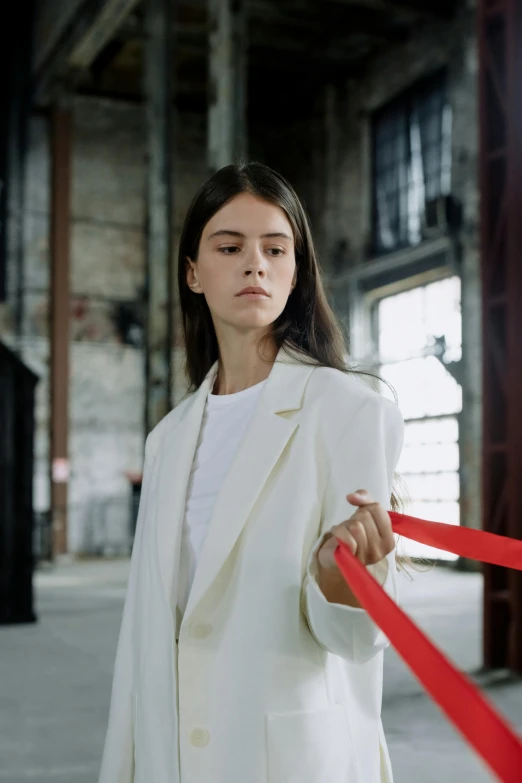 a woman in a white suit holding a red ribbon, inspired by Vanessa Beecroft, pexels contest winner, dafne keen, streetwear, ignant, brutalist fashion show