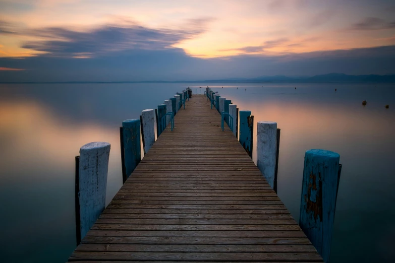 a long dock in the middle of a body of water, by Wojciech Gerson, calm evening, multicoloured, overcast, blue