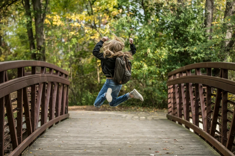 a little girl jumping in the air on a bridge, by Jesper Knudsen, pexels contest winner, happening, a backpack, avatar image, brown, natural environment