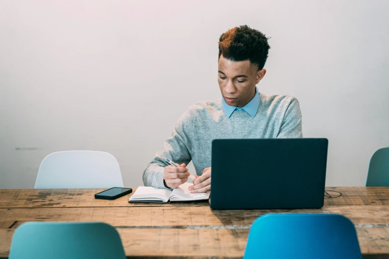 a man sitting at a table working on a laptop, pexels contest winner, young commoner, lachlan bailey, subject in middle