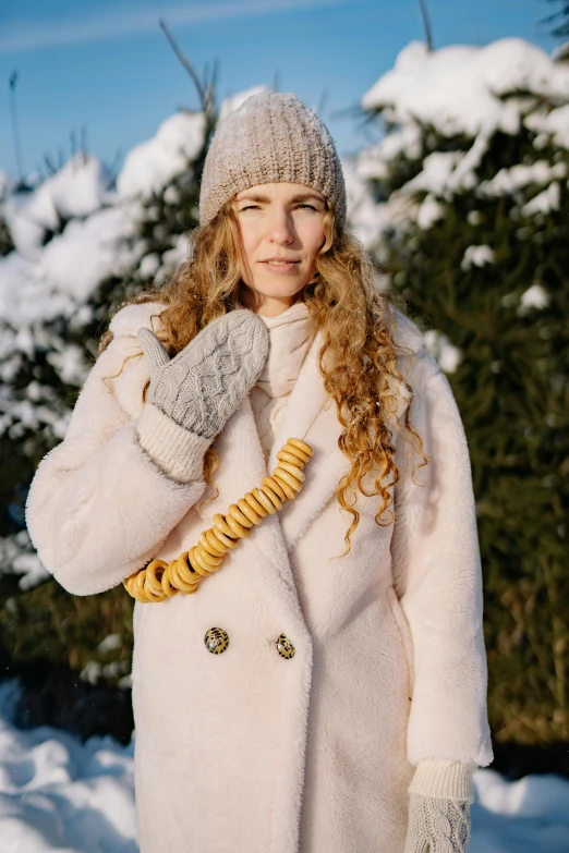 a woman in a white coat standing in the snow, a portrait, inspired by Louisa Matthíasdóttir, trending on pexels, gold accessories, mittens, wearing wool suit, curly blond