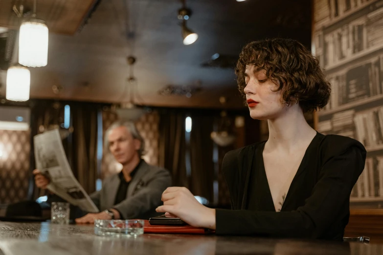 a woman sitting at a bar reading a newspaper, a portrait, by Emma Andijewska, pexels contest winner, art nouveau, man and woman, sophia lillis, serious business, medium shot of two characters