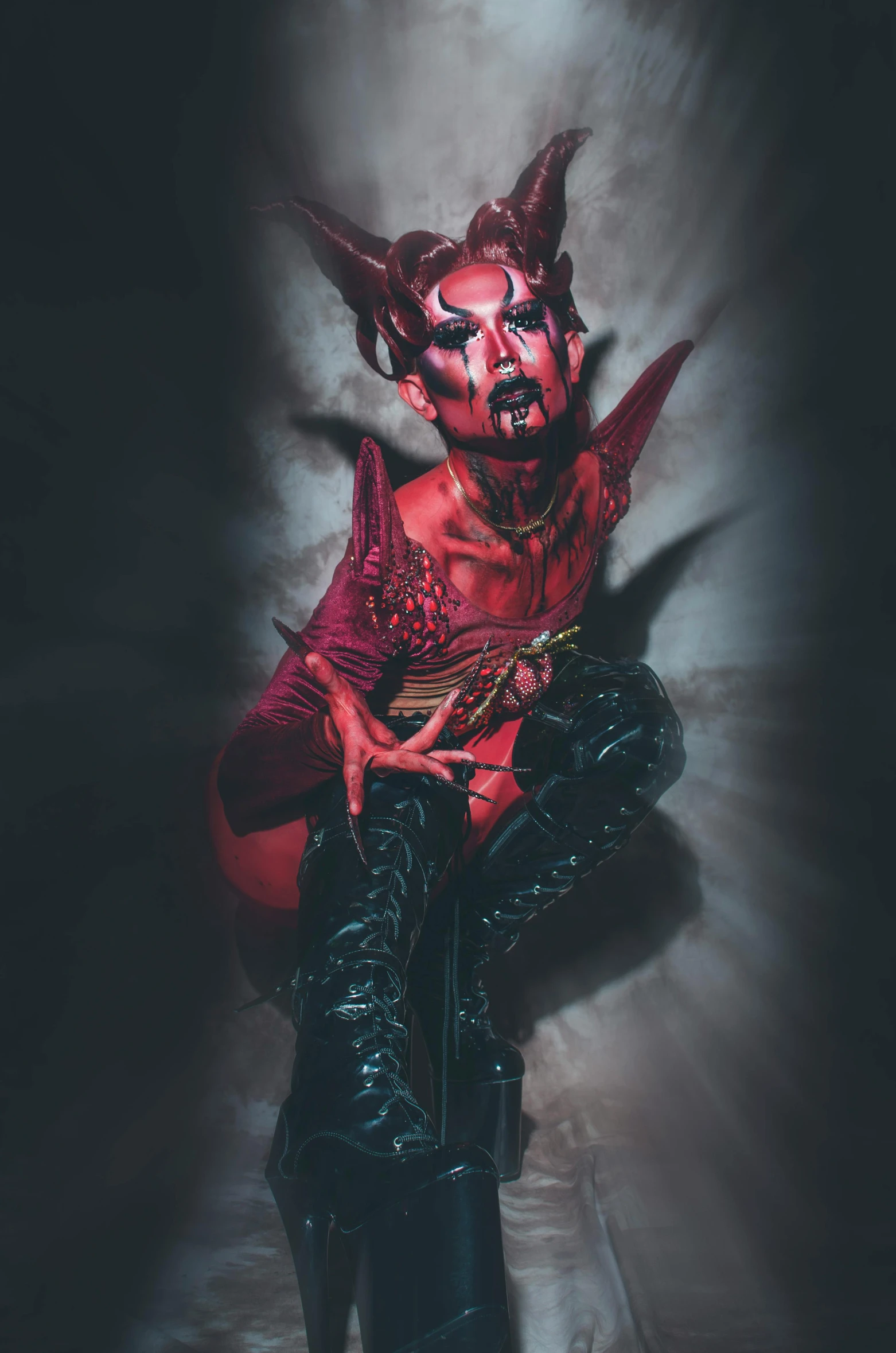 a demon sitting on top of a chair, red skin, prosthetic makeup, with horns, drag