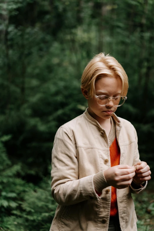 a woman standing in the woods looking at her cell phone, by Anna Boch, blond boy, wide film still, cardigan, with glasses on