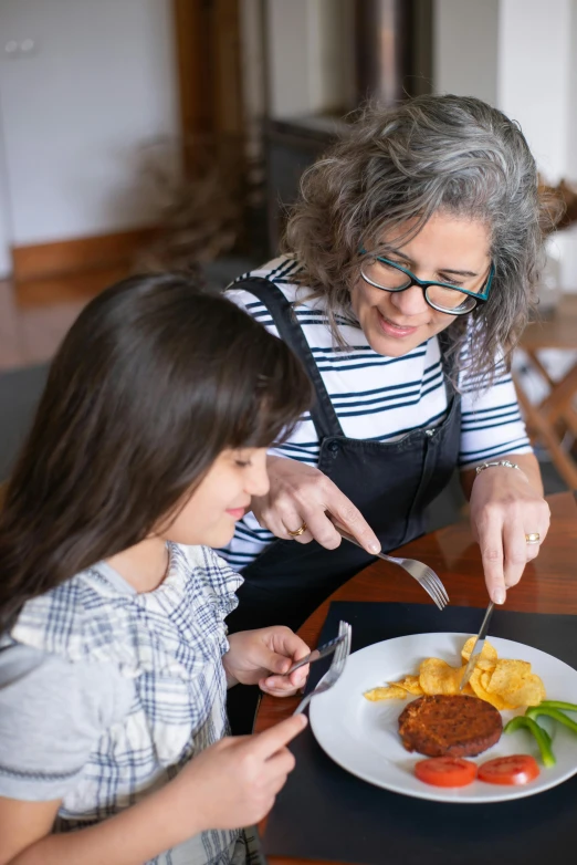 a woman and a little girl sitting at a table with a plate of food, holding a kitchen knife, plating, next gen, profile image