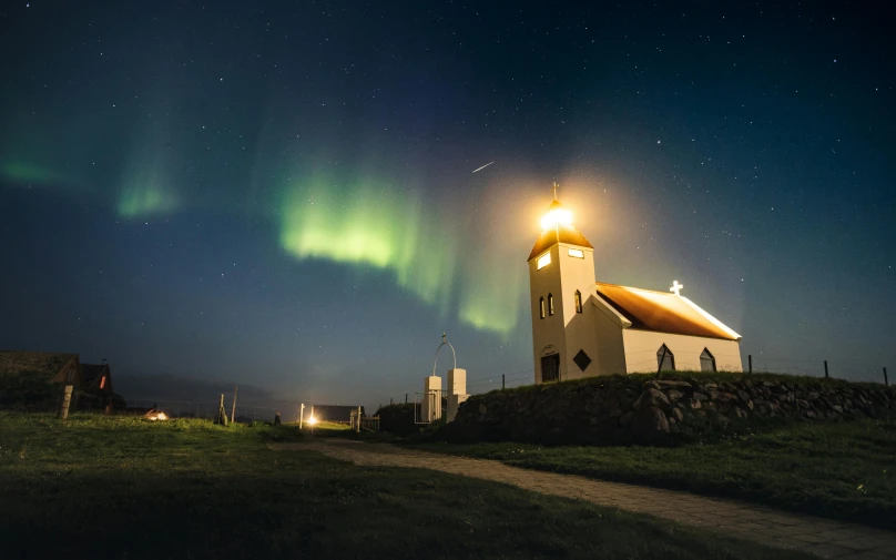 a church sitting on top of a lush green hillside, by Julia Pishtar, unsplash contest winner, northern lights in space, light house, dancing lights, album cover