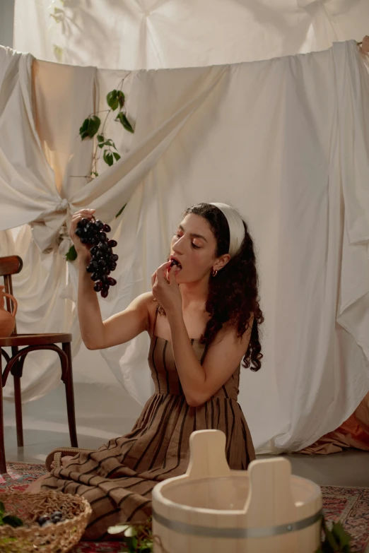 a woman sitting on the floor holding a bunch of grapes, inspired by Esaias Boursse, trending on pexels, renaissance, slurping spaghetti, on a sumptuous velvet tablecloth, olive skin, dreamy aesthetic