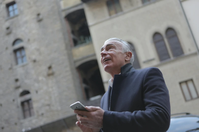 a man standing in front of a building holding a cell phone, by Francesco Filippini, with a castle in the background, jerome powell, low angle photo, florence