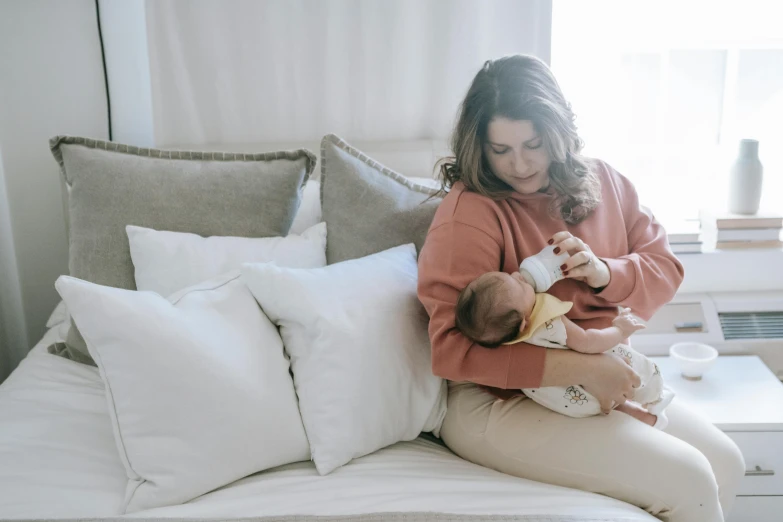 a woman sitting on a bed holding a baby, pexels contest winner, happening, milk, avatar image, brunette, comfortable atmosphere