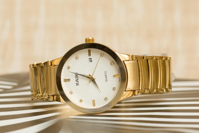 a close up of a wrist watch on a table, inspired by david rubín, pexels contest winner, accented in bright metallic gold, pulsar, plain background, a pair of ribbed