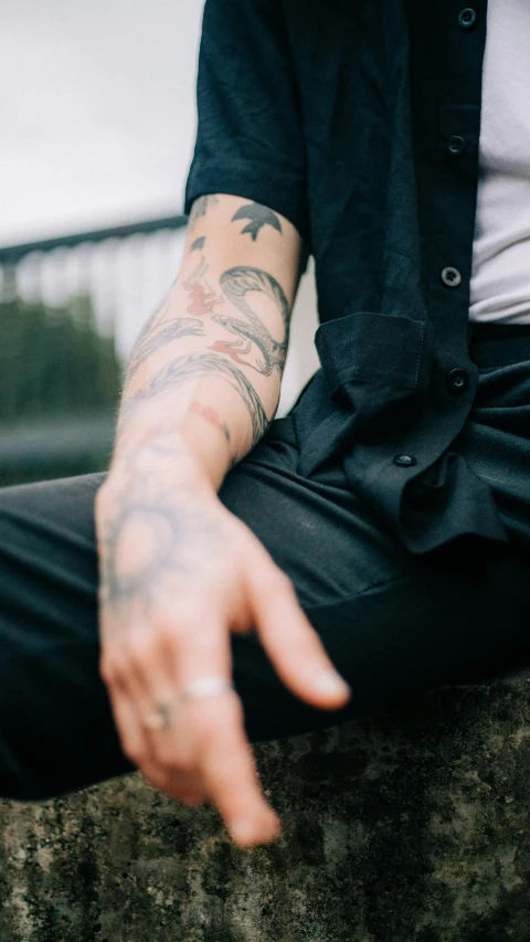 a man with tattoos sitting on a rock, a tattoo, trending on pexels, photograph of a sleeve tattoo, james jean style, zoomed out, blackwork