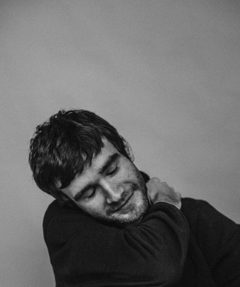 a black and white photo of a man leaning against a wall, an album cover, will graham, ethan klein, self - satisfied smirk, hasbulla magomedov