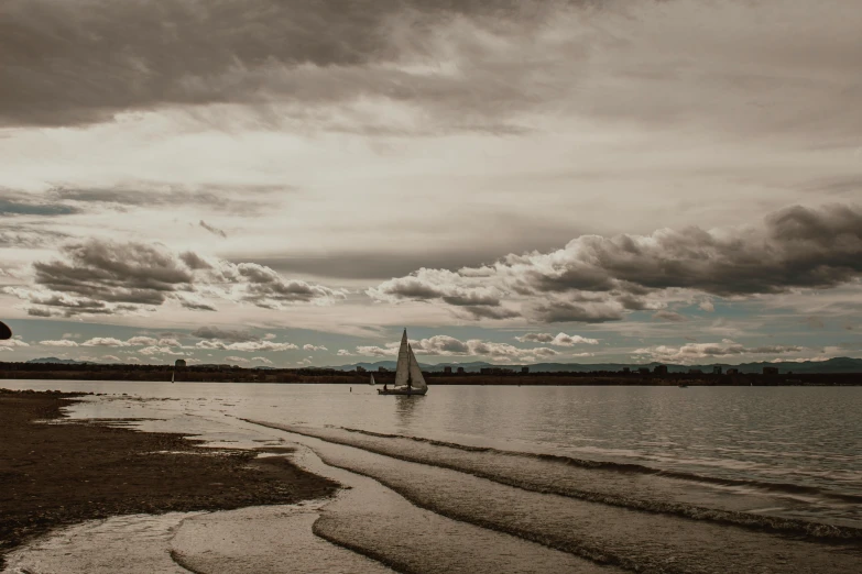 a sailboat on a body of water under a cloudy sky, by Peter Churcher, pexels contest winner, sepia colors, beach landscape, wide river and lake, a small