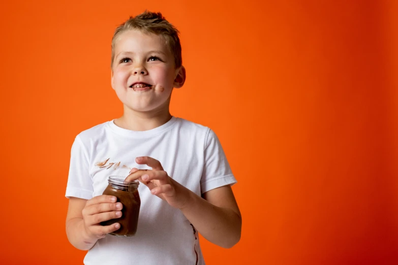 a young boy holding a jar of peanut butter, pexels contest winner, in front of an orange background, chocolate sauce, manuka, excitement