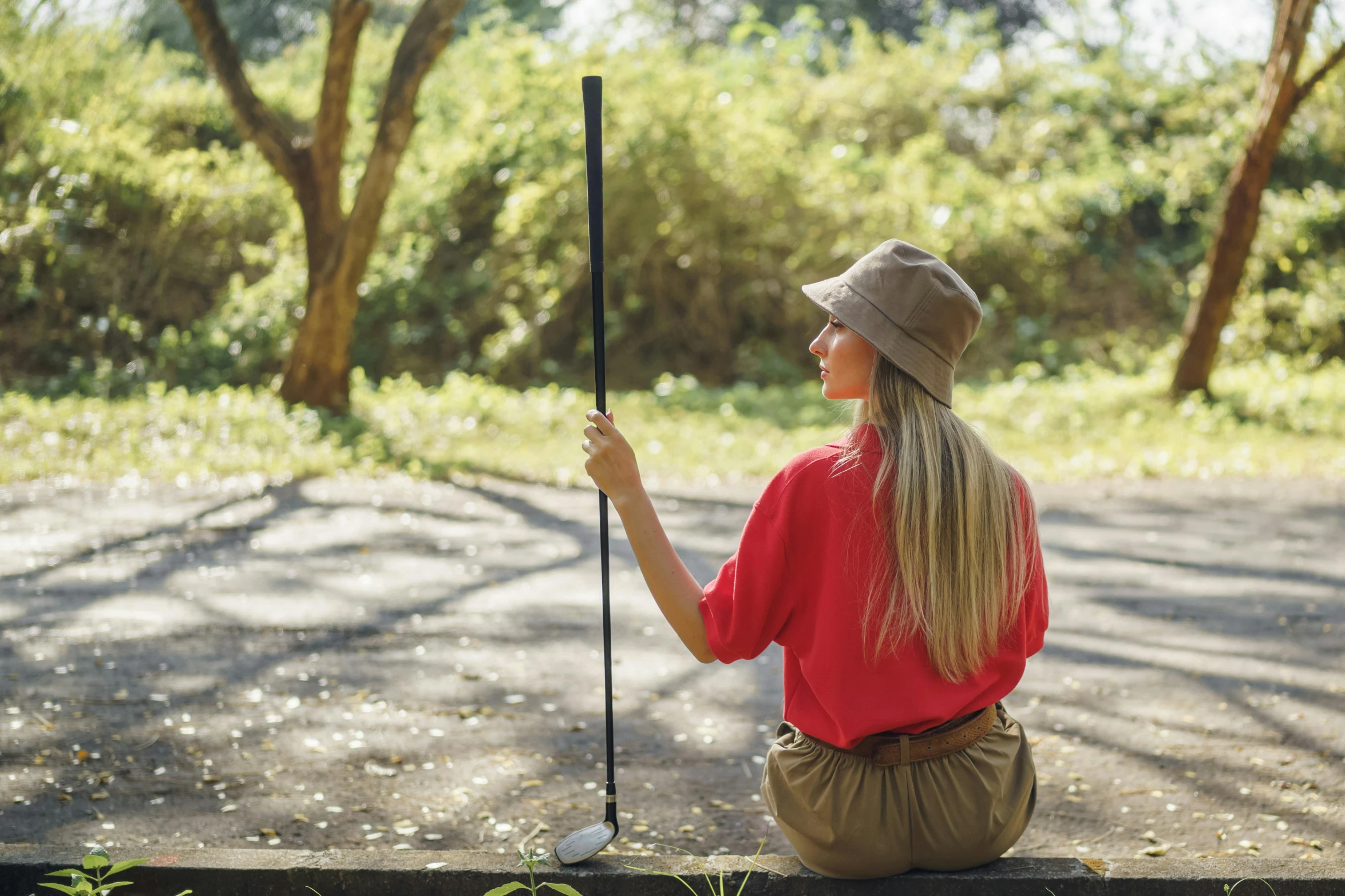 a woman sitting on a bench holding a golf club, unsplash, red hat, sydney park, avatar image, lush surroundings