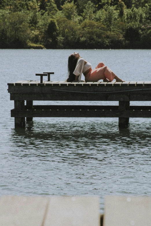 a woman laying on a dock next to a body of water, summer lake setting, **cinematic, corinne day, small dock