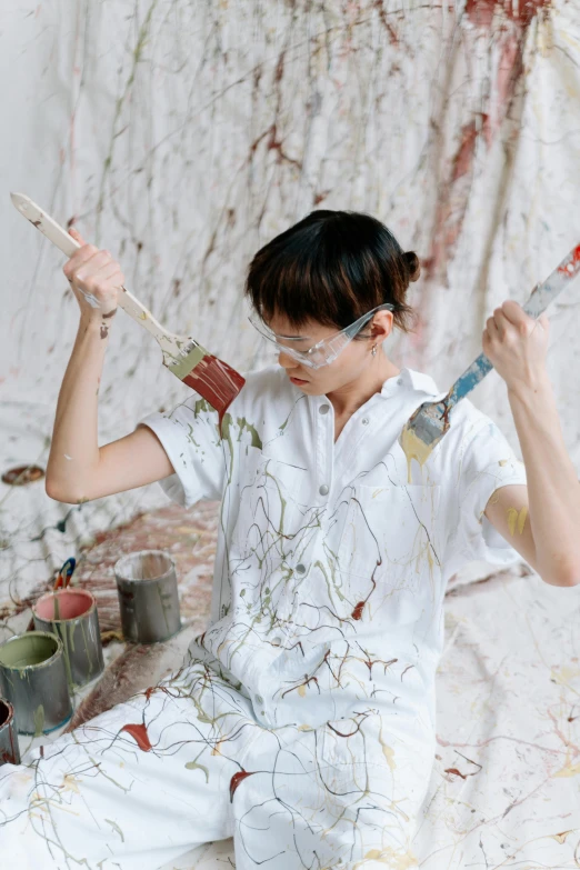 a woman sitting on the ground holding a paintbrush, inspired by Shōzō Shimamoto, trending on pexels, action painting, wearing lab coat and glasses, in white room, starving artist wearing overalls, asian man