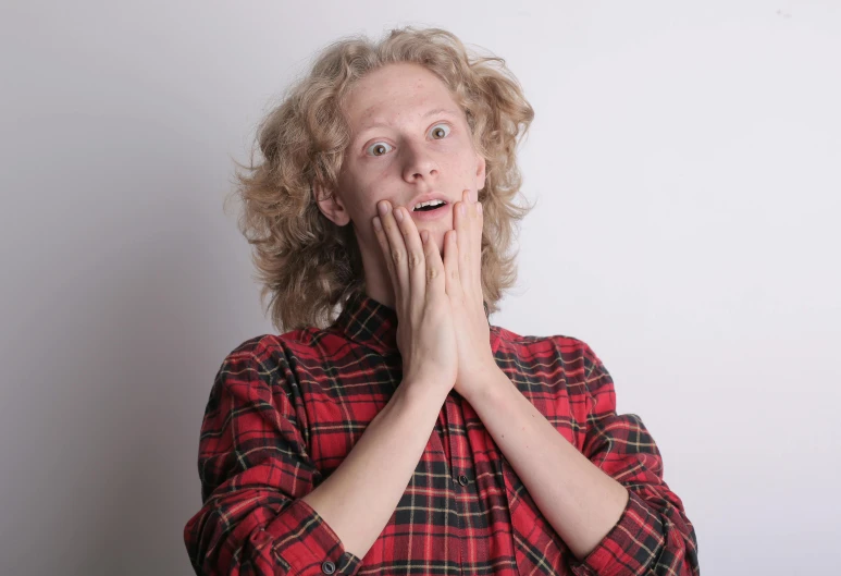 a woman with a surprised look on her face, by David Begbie, pexels, happening, wearing plaid shirt, pale skin curly blond hair, man is terrified, head in hands