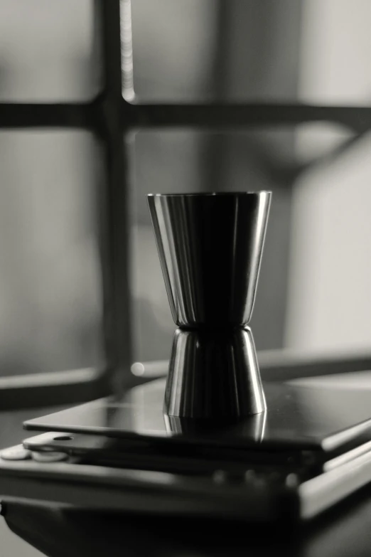 a cell phone sitting on top of a table next to a cup, a black and white photo, inspired by Robert Mapplethorpe, unsplash, purism, hourglass volumetric lighting, blurred detail, black lacquer, shot from cinematic