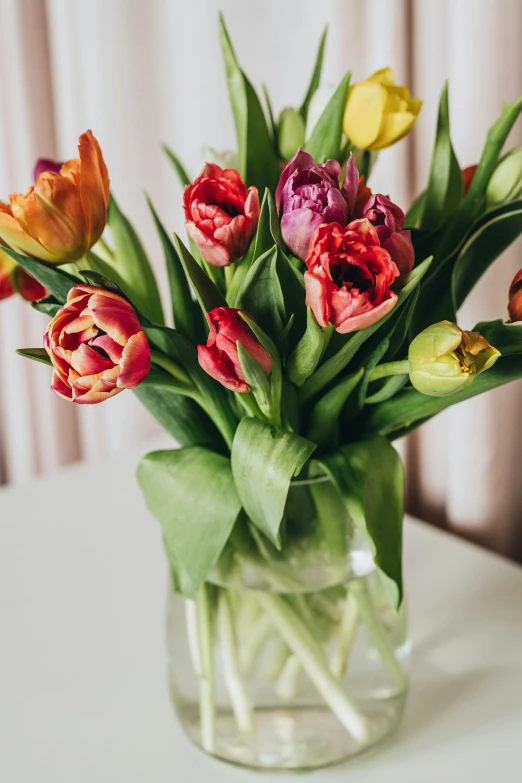 a vase filled with lots of flowers sitting on a table, tulips, iridescent accents. vibrant, casually dressed, warm hues