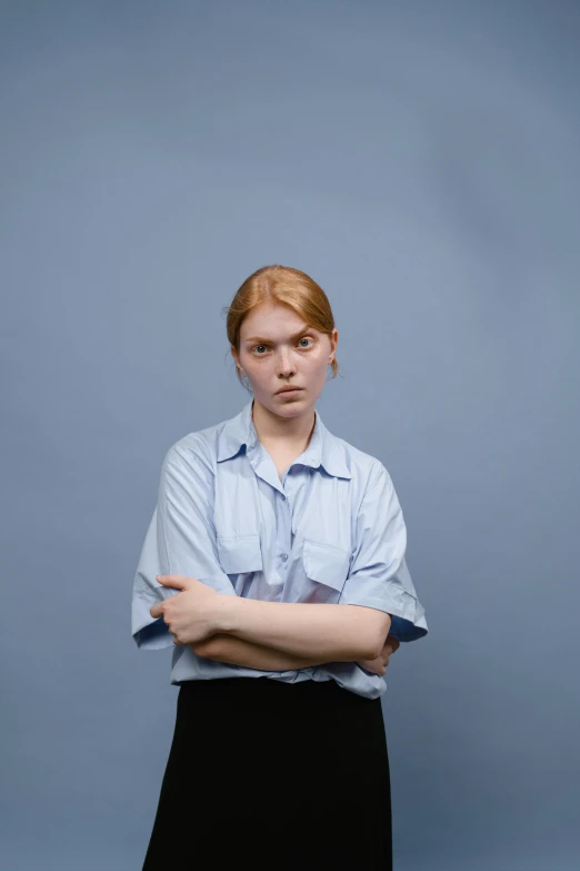 a woman in a blue shirt and black skirt, an album cover, by Lasar Segall, realism, default pose neutral expression, crossed arms, androgynous person, a redheaded young woman