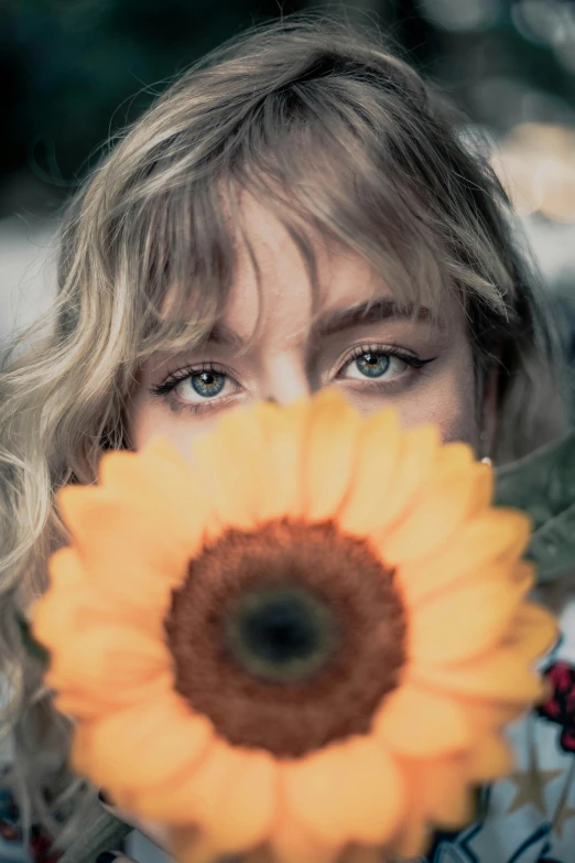 a woman holding a sunflower in front of her face, a picture, by irakli nadar, trending on pexels, portrait of kim petras, blue eyes and blond hair, icon, sydney sweeney