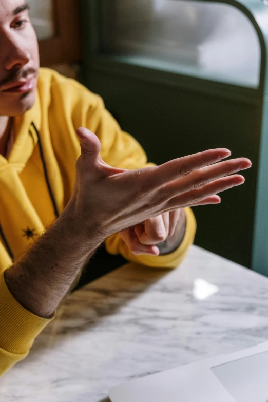 a man sitting at a table in front of a laptop, by Doug Ohlson, trending on pexels, hyperrealism, with yellow cloths, reaching out to each other, bump in form of hand, looking away