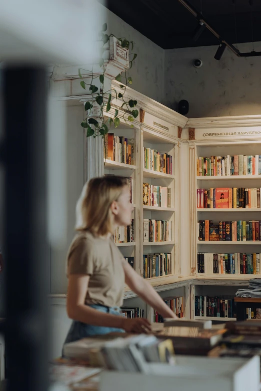 a woman standing in a kitchen next to a counter, by Oskar Lüthy, trending on unsplash, renaissance, bookshelves on sides, still frame from a movie, student, books cave