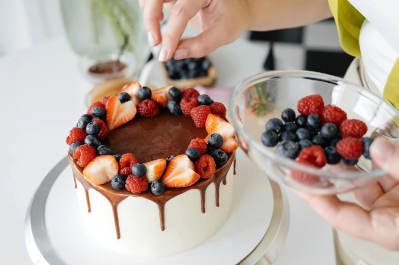 a woman is decorating a cake with berries and chocolate, pexels contest winner, 🦩🪐🐞👩🏻🦳, glazing, precision, fresh fruit