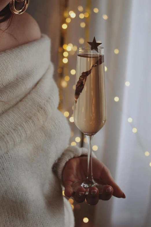 a woman in a white sweater holding a glass of champagne, a photo, inspired by Jacopo Bellini, trending on pexels, cyber copper spiral decorations, with stars, chocolate, large tall