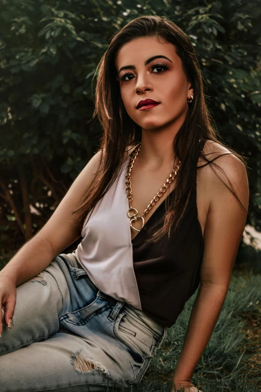 a beautiful young woman sitting on top of a lush green field, an album cover, inspired by Elsa Bleda, trending on pexels, renaissance, gold chain belt, she is wearing a black tank top, ((chains)), casual pose