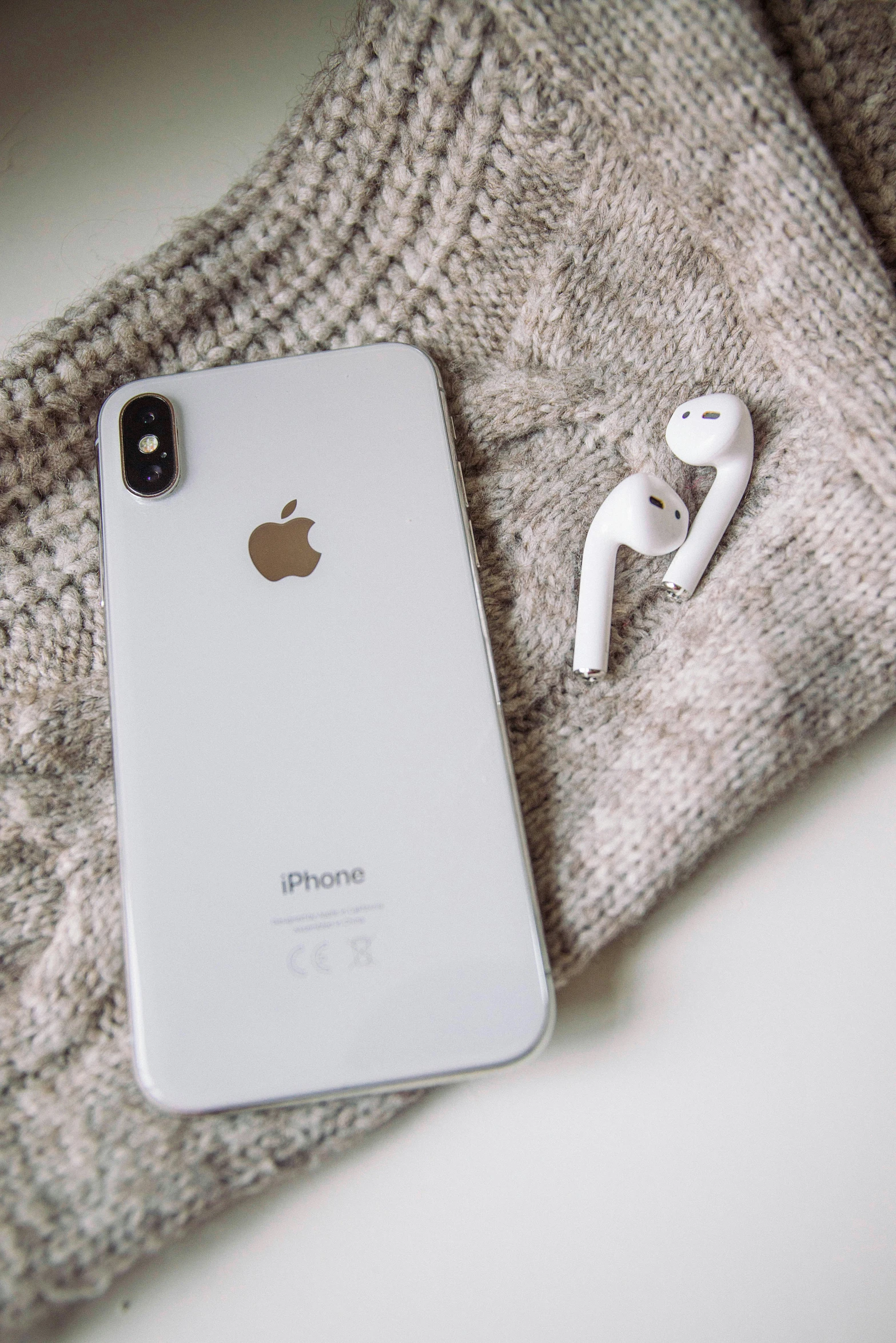 an iphone sitting on top of a sweater next to a pair of headphones, pexels, 256x256, white and silver, 8k n 9, - 9