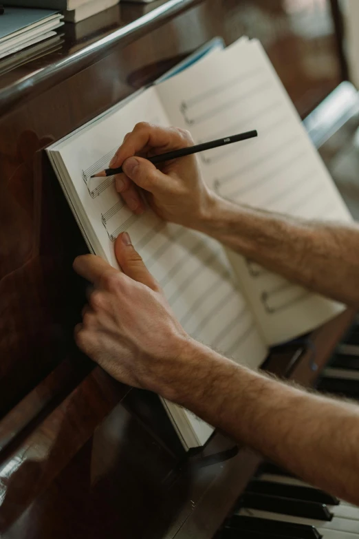 a man sitting at a piano writing on a piece of paper, an album cover, by Daniel Seghers, pexels, multiple stories, holding pencil, high quality image, made of notation